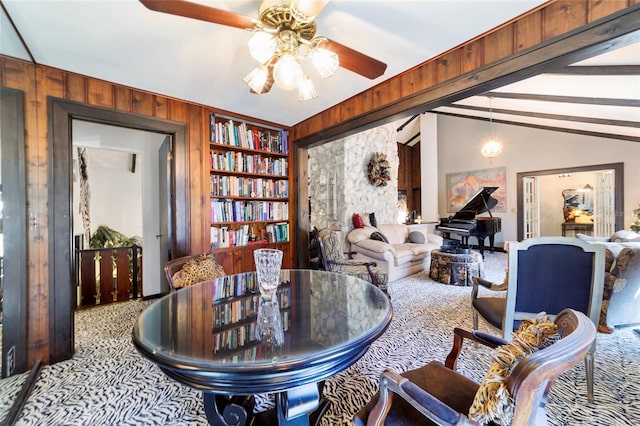 sitting room with vaulted ceiling with beams, ceiling fan, wooden walls, carpet flooring, and built in features