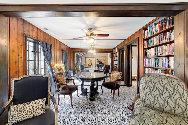 carpeted dining area with built in features, wood walls, visible vents, and a ceiling fan