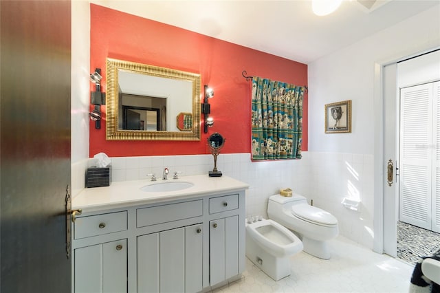 bathroom featuring wainscoting, toilet, vanity, a bidet, and tile walls