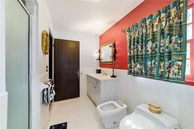 full bathroom with wainscoting, toilet, vanity, a bidet, and tile walls