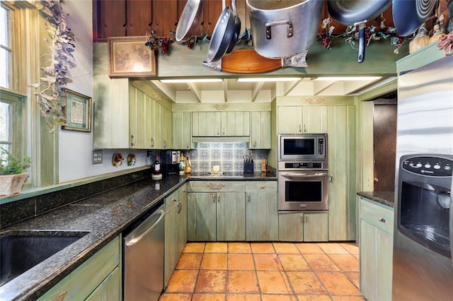 kitchen featuring backsplash, appliances with stainless steel finishes, light tile patterned flooring, a sink, and dark stone countertops