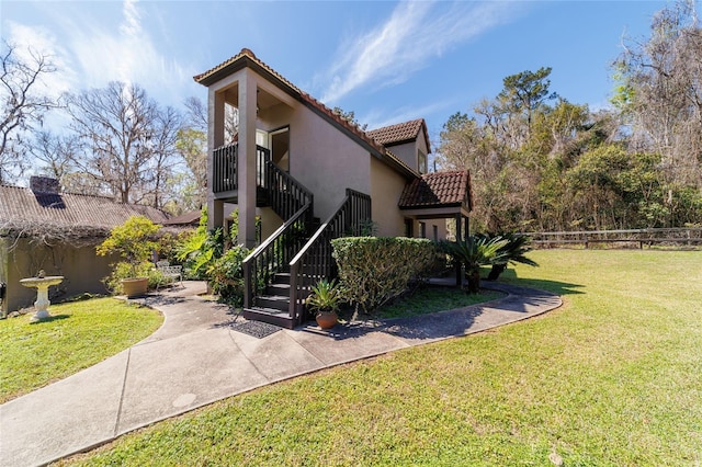 view of front of house with stucco siding, stairway, a patio area, a tiled roof, and a front lawn