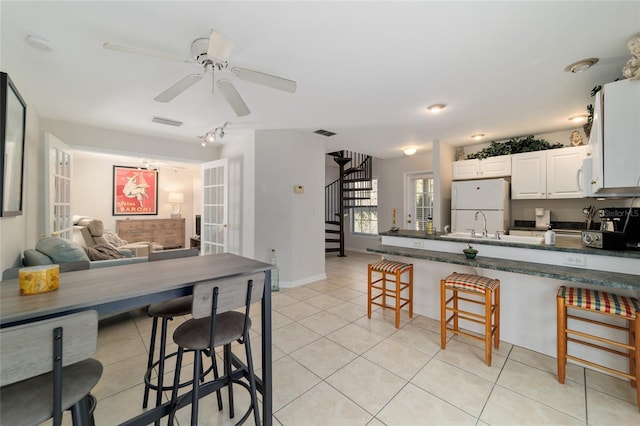 kitchen featuring light tile patterned floors, white appliances, a breakfast bar area, and dark countertops