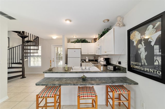 kitchen featuring white appliances, visible vents, dark countertops, a peninsula, and a sink