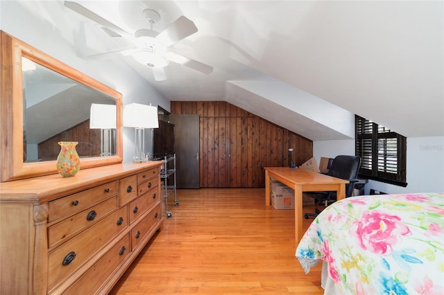 bedroom featuring light wood finished floors, lofted ceiling, visible vents, a ceiling fan, and wood walls