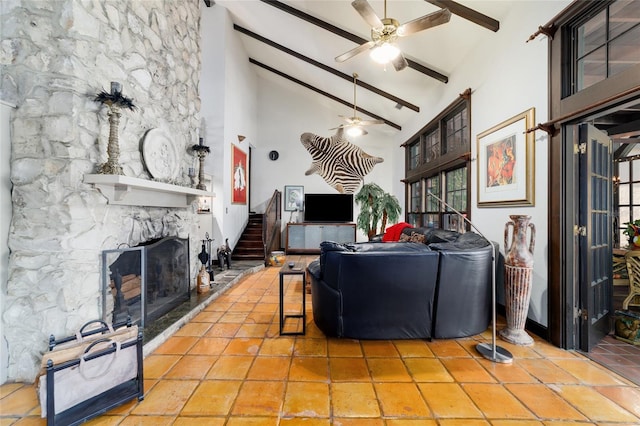 tiled living room featuring ceiling fan, high vaulted ceiling, a stone fireplace, stairway, and beamed ceiling