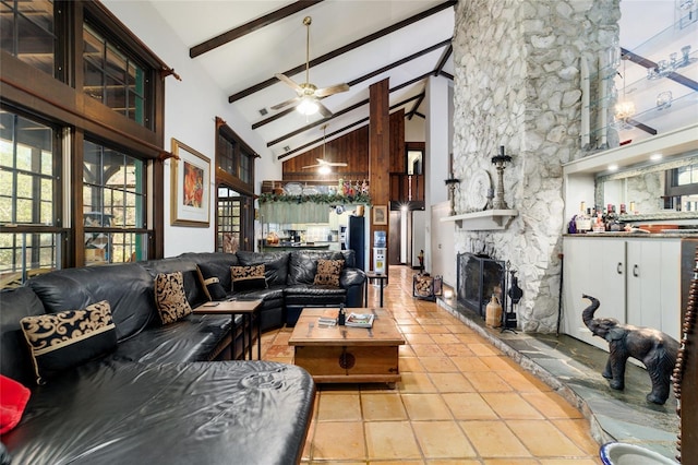 tiled living room featuring ceiling fan, high vaulted ceiling, a stone fireplace, indoor bar, and beam ceiling