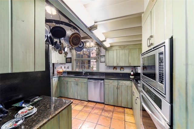 kitchen with appliances with stainless steel finishes, dark stone counters, a sink, and light tile patterned floors