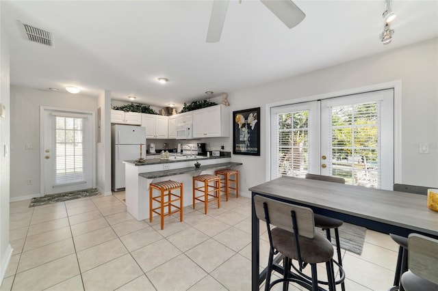 kitchen featuring light tile patterned flooring, a peninsula, white appliances, visible vents, and dark countertops