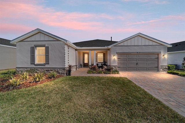 single story home with a garage, stone siding, decorative driveway, a yard, and board and batten siding