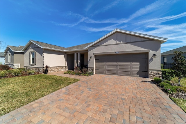 ranch-style home with a garage, stone siding, decorative driveway, stucco siding, and board and batten siding