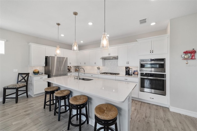 kitchen with under cabinet range hood, stainless steel appliances, a sink, backsplash, and a kitchen bar