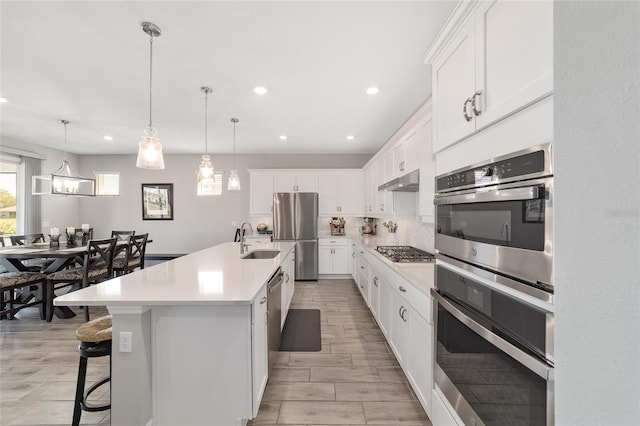 kitchen with under cabinet range hood, a sink, light countertops, appliances with stainless steel finishes, and backsplash