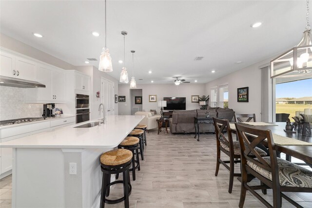 kitchen with a sink, white cabinets, light countertops, backsplash, and an island with sink