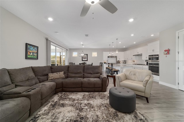 living room featuring ceiling fan with notable chandelier, baseboards, and recessed lighting