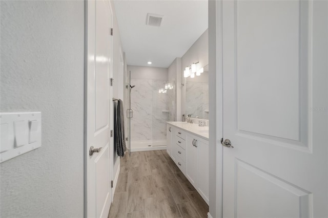 bathroom featuring a marble finish shower, visible vents, wood finished floors, and vanity