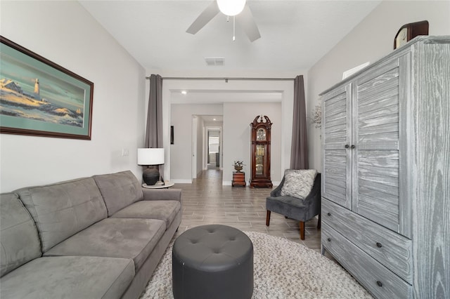 living room with a ceiling fan, visible vents, baseboards, and wood finished floors