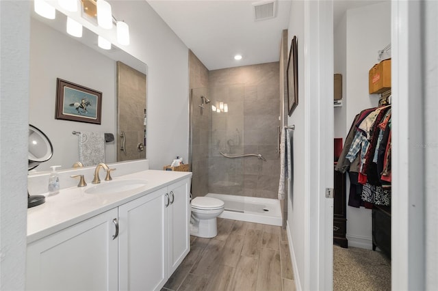 bathroom featuring wood finished floors, visible vents, vanity, a shower stall, and a walk in closet