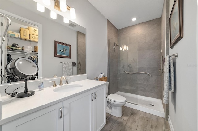 full bath featuring toilet, wood finished floors, vanity, visible vents, and a stall shower