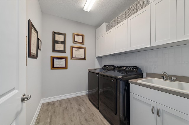 washroom featuring a textured ceiling, a sink, light wood-type flooring, cabinet space, and washing machine and clothes dryer