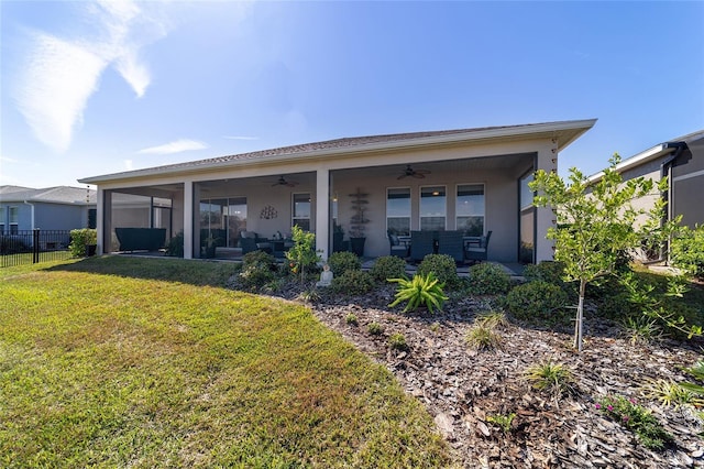 rear view of house featuring fence, a ceiling fan, a sunroom, a lawn, and stucco siding