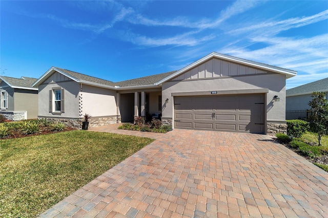 single story home with stone siding, an attached garage, decorative driveway, board and batten siding, and a front yard