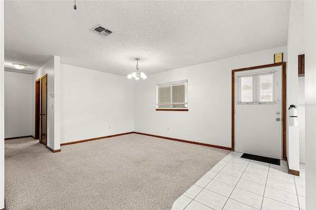 spare room featuring a chandelier, a textured ceiling, visible vents, and light colored carpet