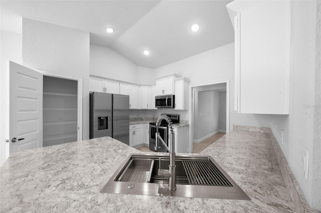 kitchen featuring white cabinets, lofted ceiling, appliances with stainless steel finishes, a sink, and recessed lighting