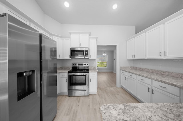 kitchen with light stone countertops, light wood-style flooring, appliances with stainless steel finishes, and white cabinets