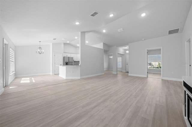 unfurnished living room with light wood-type flooring, vaulted ceiling, visible vents, and a chandelier