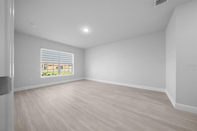 empty room with light wood finished floors, visible vents, and baseboards