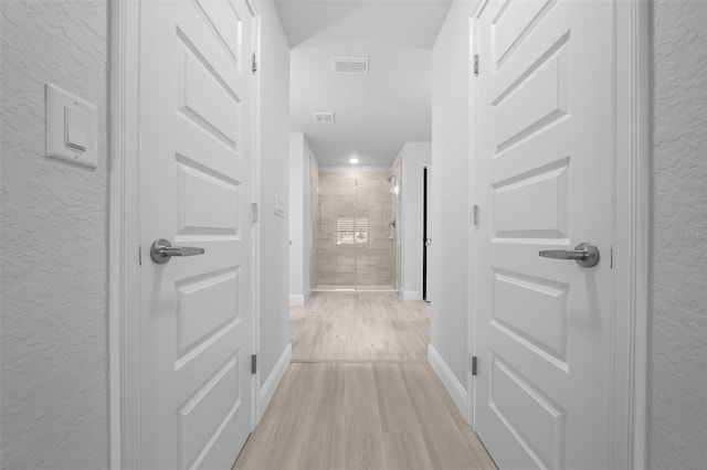 hall featuring a textured wall, light wood-style flooring, visible vents, and baseboards