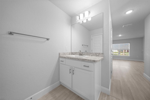 bathroom featuring a textured wall, wood finished floors, vanity, and baseboards