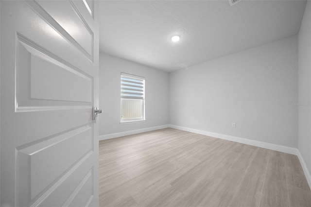 empty room with light wood-style floors, baseboards, and a textured ceiling