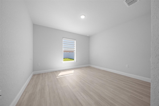 unfurnished room with light wood finished floors, visible vents, and baseboards