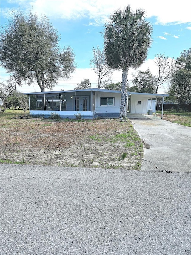 single story home featuring concrete driveway, a carport, and a sunroom