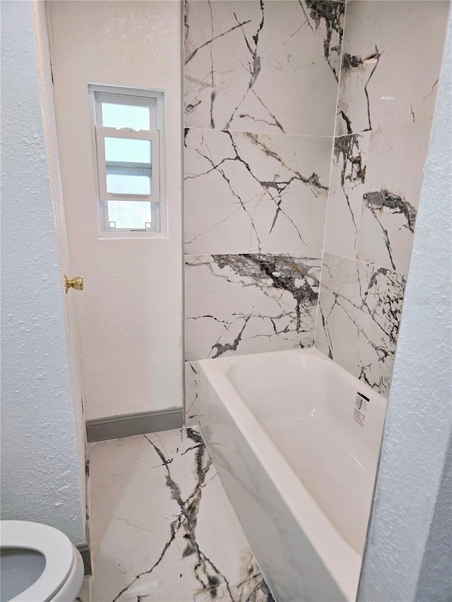 bathroom with marble finish floor, a textured wall, toilet, and a bath