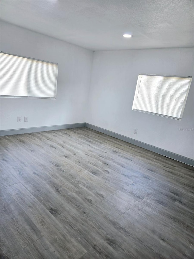 unfurnished room with a textured ceiling, baseboards, wood finished floors, and recessed lighting