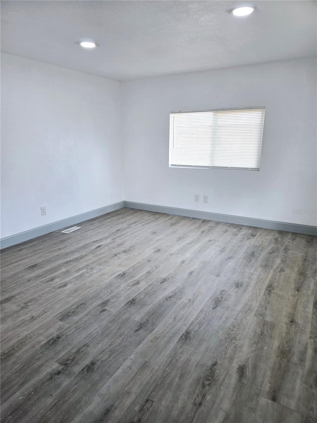 spare room with a textured ceiling, recessed lighting, wood finished floors, and baseboards