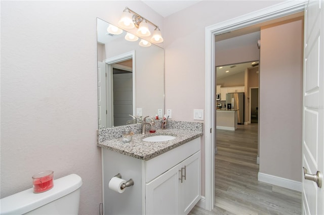 half bathroom with vanity, baseboards, wood finished floors, and toilet