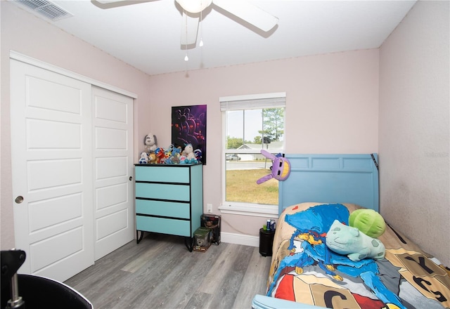bedroom with ceiling fan, visible vents, wood finished floors, and a closet