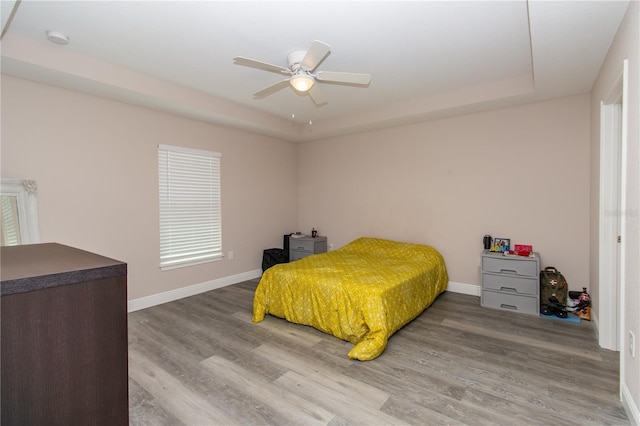 bedroom with a ceiling fan, baseboards, wood finished floors, and a raised ceiling