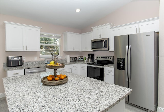 kitchen with vaulted ceiling, white cabinets, a kitchen island, and stainless steel appliances