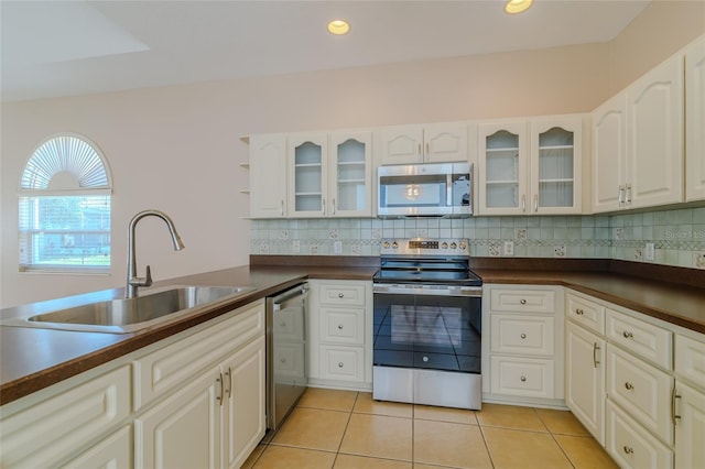 kitchen with tasteful backsplash, dark countertops, appliances with stainless steel finishes, a sink, and light tile patterned flooring