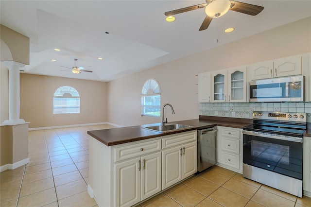 kitchen with stainless steel appliances, dark countertops, a sink, and ornate columns