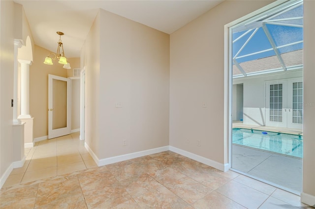 empty room featuring french doors, decorative columns, an inviting chandelier, light tile patterned flooring, and baseboards