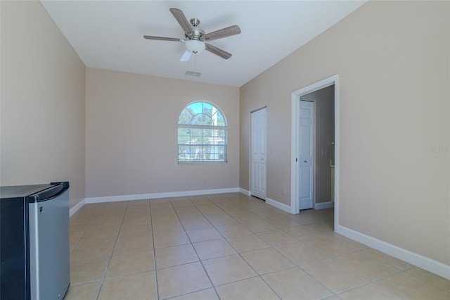 empty room featuring light tile patterned floors, baseboards, visible vents, and a ceiling fan