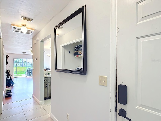 corridor with light tile patterned floors, baseboards, visible vents, and a textured ceiling