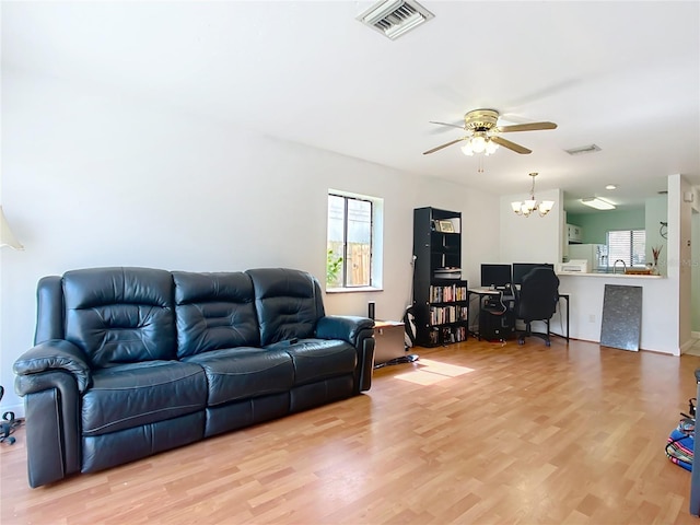 living area with ceiling fan with notable chandelier, light wood finished floors, and visible vents