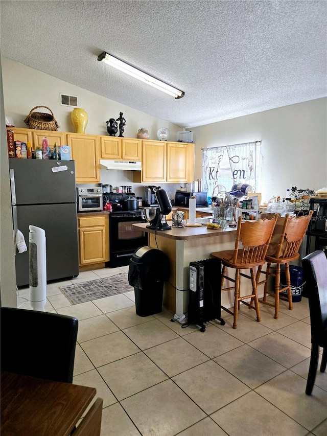 kitchen with electric range, light tile patterned floors, freestanding refrigerator, and light brown cabinetry